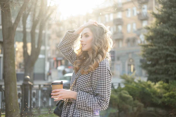 Женщина в плаще ходьба и пить кофе из бумажной чашки — стоковое фото