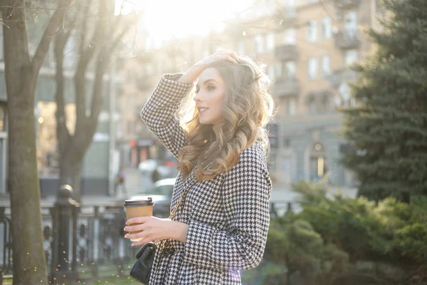 Mujer en gabardina caminando y bebiendo café de taza de papel — Foto de Stock