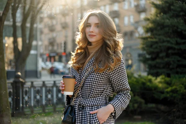 Mujer en gabardina caminando y bebiendo café de taza de papel —  Fotos de Stock