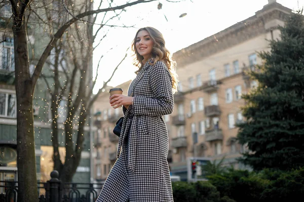 Frau im Trenchcoat geht und trinkt Kaffee aus Pappbecher — Stockfoto