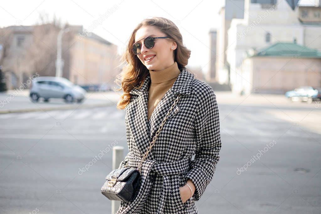 Attractive girl in a coat in the street in a city, sun is shining