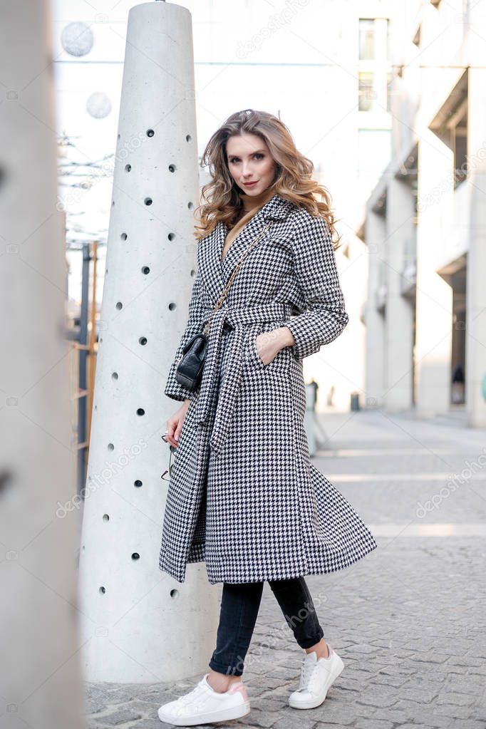 Attractive girl in a coat in the street in a city, sun is shining