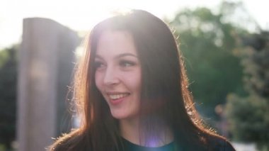 Şehrin gün batımının arka planında güzel bir genç kadının portresi. Şehirde sokakta yürüyen deri ceketli çekici kız, güneş bahar güneşini parlatıyor. Yavaş çekim