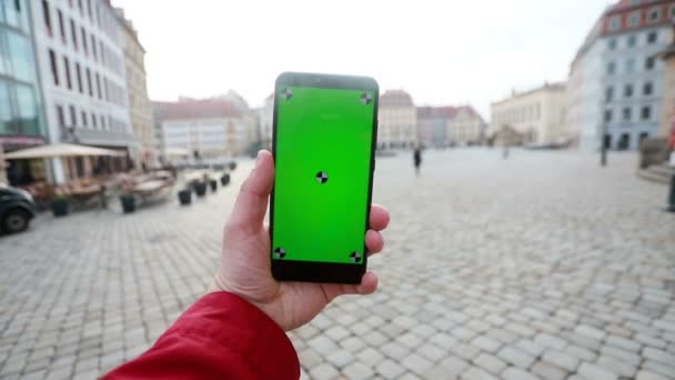 街の通り背景に緑色の画面を持つスマート フォンを保持している男の手のショットを閉じる クロマ — ストック動画