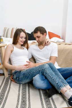 Çocuğu bekleyen genç bir çiftin portresi. Bir çiftin mutlu bir şekilde kameraya gülüşünü, karnındaki bebeği kucaklayışını..