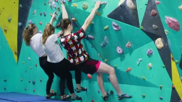 フィットネス 極端なスポーツ ボルダリング 人々と健康的なライフスタイルの概念 3人の女性が人工的な壁を登っています 室内で極端なレジャーを楽しむ岩をつかむプロの登山家の女性 — ストック動画