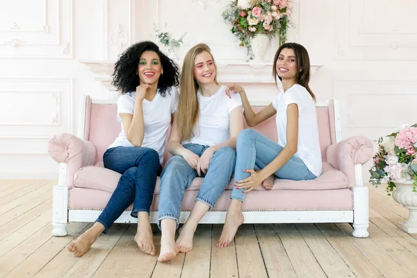 friendship and happiness concept - three girlfriends having a talk at home. Three happy funny multi ethnic ladies best friends laughing having fun, pretty diverse women wear white t-shirts and jeans