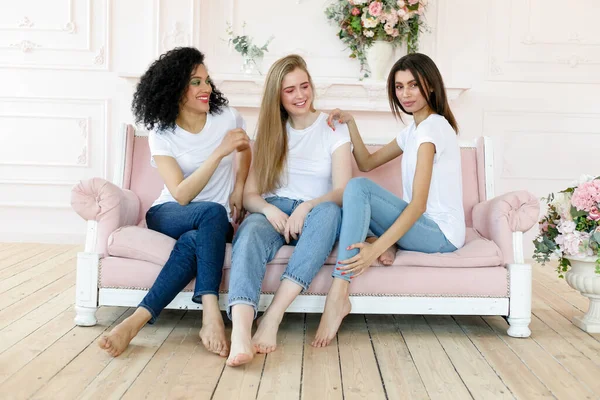 friendship and happiness concept - three girlfriends having a talk at home. Three happy funny multi ethnic ladies best friends laughing having fun, pretty diverse women wear white t-shirts and jeans