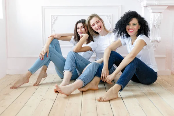 friendship and happiness concept - three girlfriends having a talk at home. Three happy funny multi ethnic ladies best friends laughing having fun, pretty diverse women wear white t-shirts and jeans