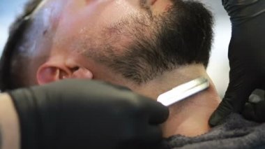 Profesyonel berber, müşteri sakalını ustura ile tıraş eder. Berber dükkanında eski moda bıçakla kesilmiş bir sakal. Yakışıklı maço adam stüdyoda sakalını kestiriyor. Yakın çekim..
