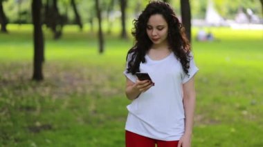 Bir yaz parkındaki rahat genç bayanın portresi cep telefonundan mesaj okuyor. Koyu kıvırcık saçlı güzel bir kız cep telefonunu açık havada kullanıyor..