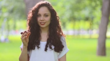 Günışığı, kıvırcık saçlı, gülümseyen genç kadın, kameraya bak, gülümse, parkta gülümse, gülümse, mutlu, yavaş çekimde yaz güneşi, gün batımına bak.