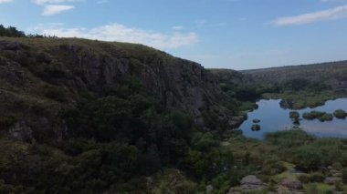 Bir dağ nehrinin havadan çekilmiş görüntüsü, bir dağın üzerinden geriye doğru uçuyor, gün batımında yeşil nehir kıyısından geçiyor, akıntılı küçük kayalar, su yüzeyinde güneş ışığı