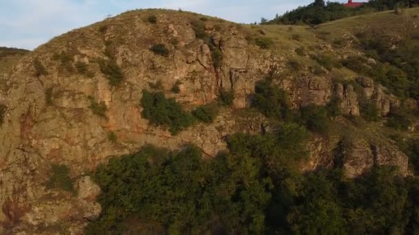 空中摄影无人驾驶飞机拍摄山河 向后飞越一座山 夕阳西下经过绿河岸 小岩石喷出急流 水面阳光普照 — 图库视频影像