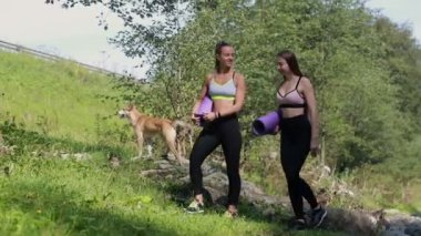 Dağlarda yürüyen, yoga minderleri tutan iki neşeli kadın. Gülümseyen kadın arkadaşlar dışarıda antreman yapıyorlar. Yoga çalış, pilates yap.