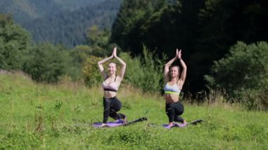 Güzel vücutlu iki güzel bayan birlikte yoga yapıyorlar dağlarla güzel bir doğa manzarasında yoga yapıyorlar, pilates yapıyorlar.