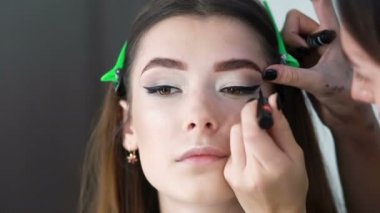 Güzellik salonundaki kız makyaj yapıyor. Kadının dudakları kaşlarla boyanmış. Temel tozunu kozmetik fırçayla uygula.