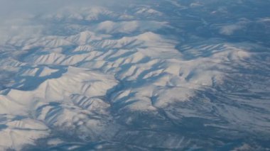 Uçak uçuşu. Gün batımı gökyüzü ile bulutların üzerinde uçan bir uçağın kanadı. Uçağın penceresinden bak. Uçak, uçak. Hava yoluyla seyahat etmek. Karla kaplı dağlar, manzaralar. 4K UHD videosu
