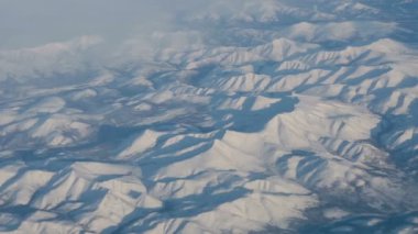 Uçak uçuşu. Gün batımı gökyüzü ile bulutların üzerinde uçan bir uçağın kanadı. Uçağın penceresinden bak. Uçak, uçak. Hava yoluyla seyahat etmek. Karla kaplı dağlar, manzaralar. 4K UHD videosu