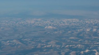 Uçak uçuşu. Gün batımı gökyüzü ile bulutların üzerinde uçan bir uçağın kanadı. Uçağın penceresinden bak. Uçak, uçak. Hava yoluyla seyahat etmek. Karla kaplı dağlar, manzaralar. 4K UHD videosu