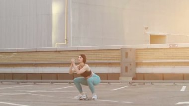 spor, fitness ve sağlıklı yaşam tarzı konsepti - spor yapan genç bir kadın ağır çekimde dışarıda çömeliyor. Atletik kadın antrenmanı ve gün batımında elastik bantla fiziksel egzersiz..