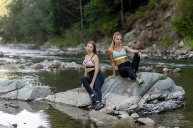 Fitness, spor, yoga ve sağlıklı yaşam tarzı konsepti. Spor yaptıktan sonra çayırlarda oturan mutlu bayan arkadaşlar. Spor yapan kadınlar birlikte oturup, spor yaptıktan sonra dinleniyorlar..