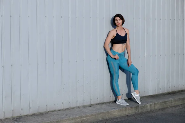 Tough young woman in sports wear staring at camera. Sportswoman taking a breather after training outdoors.