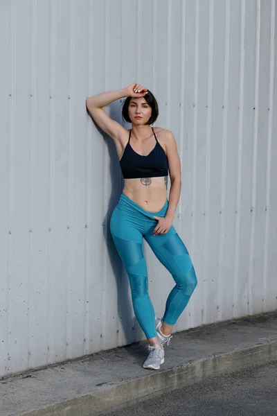 Tough young woman in sports wear staring at camera. Sportswoman taking a breather after training outdoors.