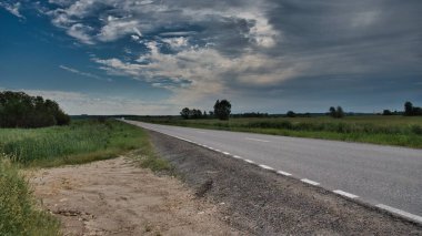 Küçük beyaz bir araba, yaklaşan havadan tarlaların arasından geçen bir yolda gidiyor.