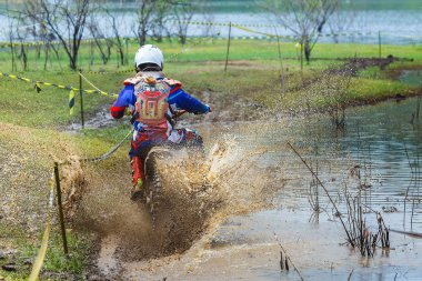 Enduro çamurun içinde yüzüyor, şoför ıslak ve çamurlu araziye çamur sıçrıyor, motokros yarışçısı sürücüyü tamamen kaplıyor..