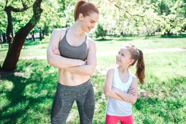 Genç ve ince bir kadın ve kızı parkta duran güzel resim. Onlar birbirine bakarak ve gülümseyerek. Kız geçti ellerini tutmak. Yoga ve Pilates kavramı. Yoga ve Pilates