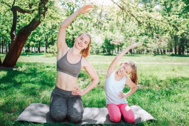 Küçük kız ecxercise annesine tekrarlıyor. Kalça üzerinde sol el tutuyorlar ve sağ el havada doldu. Sola doğru bükme. Yoga ve Pilates kavramı.