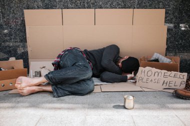 Çaresiz ve savunmasız adam karton beton zemin üzerine yalan ve uyku. O Güneş'ten gizleme elleriyle yüzünü koruyor. Onu yanında bir işareti diyor evsizlere yardım lütfen.
