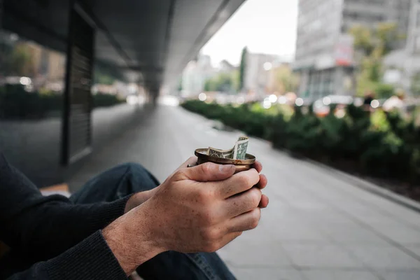 En piture av mans händer som håller en kopp med en proposition. Han är en tiggare. Killen sitter på marken utanför. Han är ensam. — Stockfoto