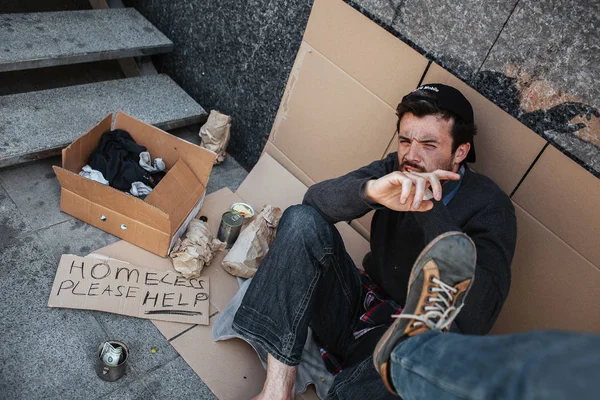 Tiggare sitter på betonggolvet och försöka försvar själv eftersom dessa är någons ben som vill stämpla tiggare. Han är hjälplös och rädd. — Stockfoto