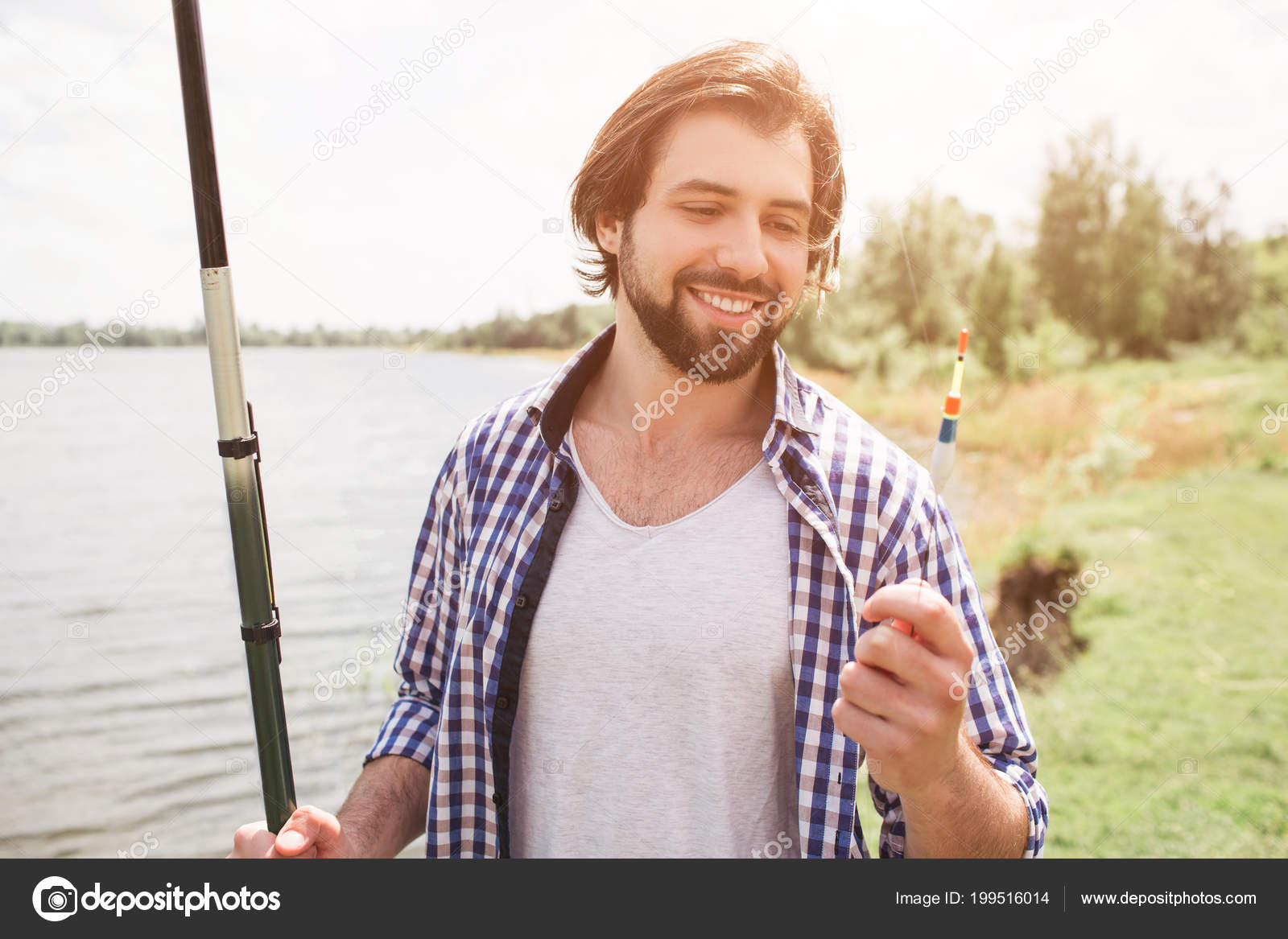 Calm and thoughtful guy is standing at the edge of lake and looking at it.  He