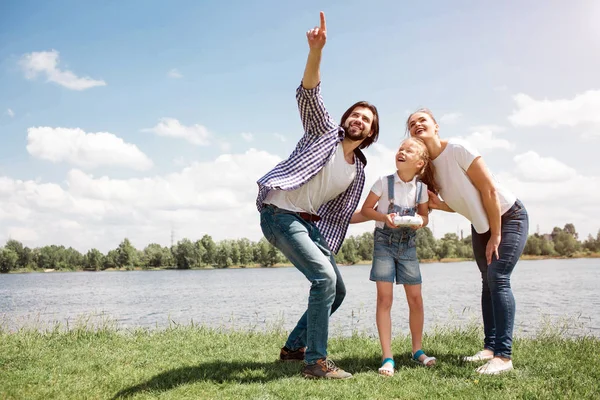 Pěkný obrázek mladé rodiny vzhlédl obloze. Guy směřuje nahoru. Dívka má ovládací panel na rukou. Rodiče se drží své dcery zpět. Oni jsou šťastní. — Stock fotografie