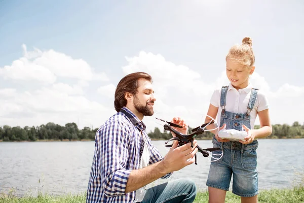 Obrázek otce a dcery spolu trávili čas. Chlap drží DRONY a ukazuje, že dívce, zatímco malé dítě má ovládací panel v jejích rukou. Dítě se dívá na DRONY a také. — Stock fotografie