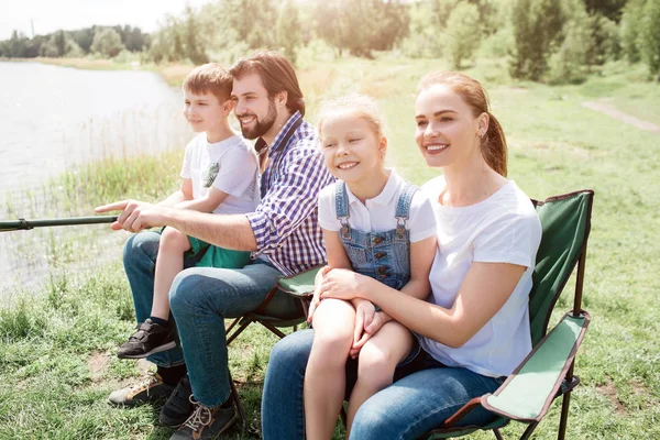 Nice family picture of four people catching fish together. Small girl is sitting on her mamas lap while small boy is doing the same thing but on his daddys lap. Boys are holding fish-rod togther.
