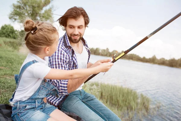 Une photo d'une fille interrogeant son père sur la pêche pendant un moment. Elle veut prendre la canne à poisson entre ses mains et le faire toute seule. Il la regarde et lui donne sa canne à poisson. Il aime sa fille. . — Photo