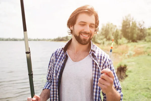 Спокійний і вдумливий хлопець стоїть на краю озера і дивиться на нього. Він тримає рибний рукав на правому плечі правою рукою. Є гарна погода . — стокове фото