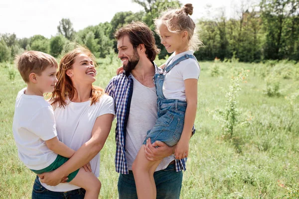 Una foto de una familia amigable. El hombre y Woamn tienen a los niños en sus manos. Se miran unos a otros con amor incondicional. Todos son muy felices. . — Foto de Stock