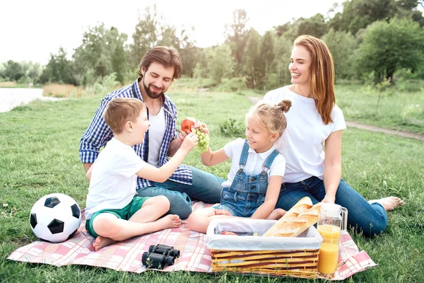 La gente de una familia está sentada junta y divirtiéndose. Los niños están partiendo uvas mientras el hombre tiene una manzana en la mano. La mujer lo mira y se ríe. . — Foto de Stock