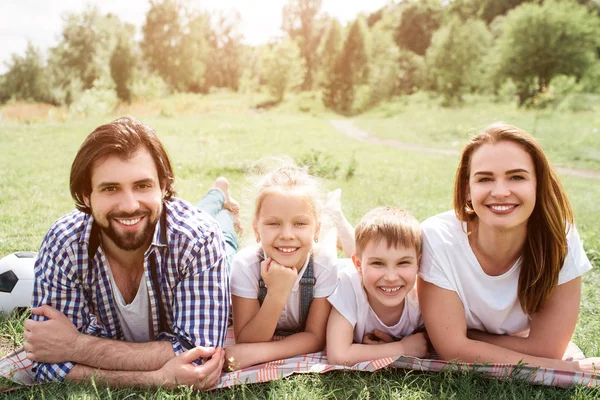 Todos los miembros de la familia están acostados juntos sobre una manta. Están mirando a la cámara y sonriendo . — Foto de Stock