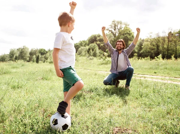 Papá está gritando y gritando. Está muy contento por su hijo. El chico jugó un buen juego. Ganó. Niño está de pie junto a su padre y la celebración de la pelota con la pierna . — Foto de Stock