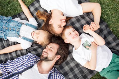 Muhteşem aile üyeleri battaniye çim üzerinde yalan söylüyorsun. Adam kız arıyor. Kadın oğlu arıyor. Onlar gülümseyen ve gülüyor. Aile speding birlikte tam zamanı.