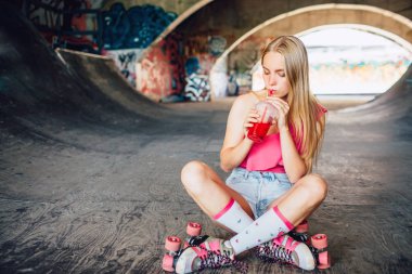 Yorgun ve güzel kız oturuyor ve kepping bacaklarını geçti. Plastik bardak kırmızı suyu içiyor. Kız üzerinde yoğunlaşmıştır. Uzun egzersiz sonrası dinleniyor.