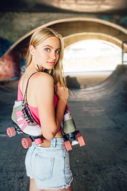 Güzel ve kendine güvenen kız kameraya poz dikey resim. O ayakta ve geriye dönüp baktığımda. Onun omzunda asılı silindirler kız tutar.