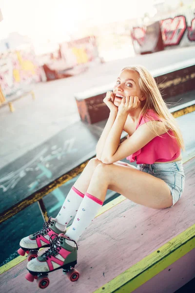 Pionowe Zdjęcie modelu Blondynka nosi rolki i szorty z bluzka. Ona trzyma ręce na podbródek i patrząc na kamery. Siedzi i pozowanie. — Zdjęcie stockowe