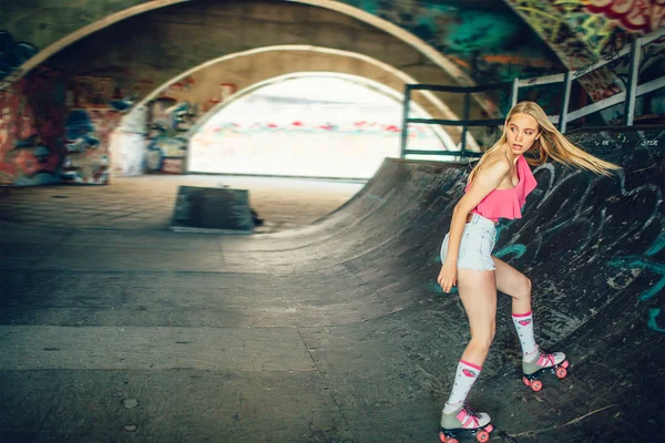 Menina loira bonita e bem construída está patinando na sala de treinamento especial. Ela está a ir para trás. A rapariga está a olhar para trás com uma visão séria. Ela está concentrada. . — Fotografia de Stock